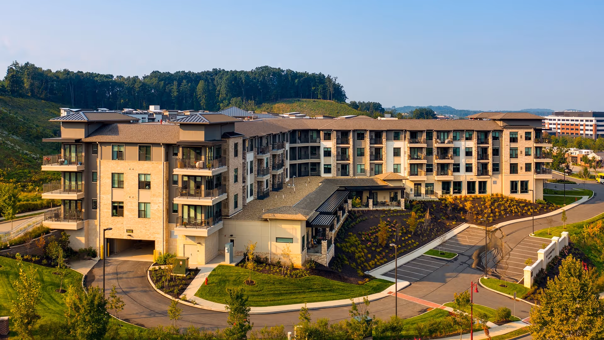 Aerial view of Ridgecrest at Cranberry Woods, a large multi-story senior living facility surrounded by landscaped greenery, parking areas, and hills in the background under a clear sky.