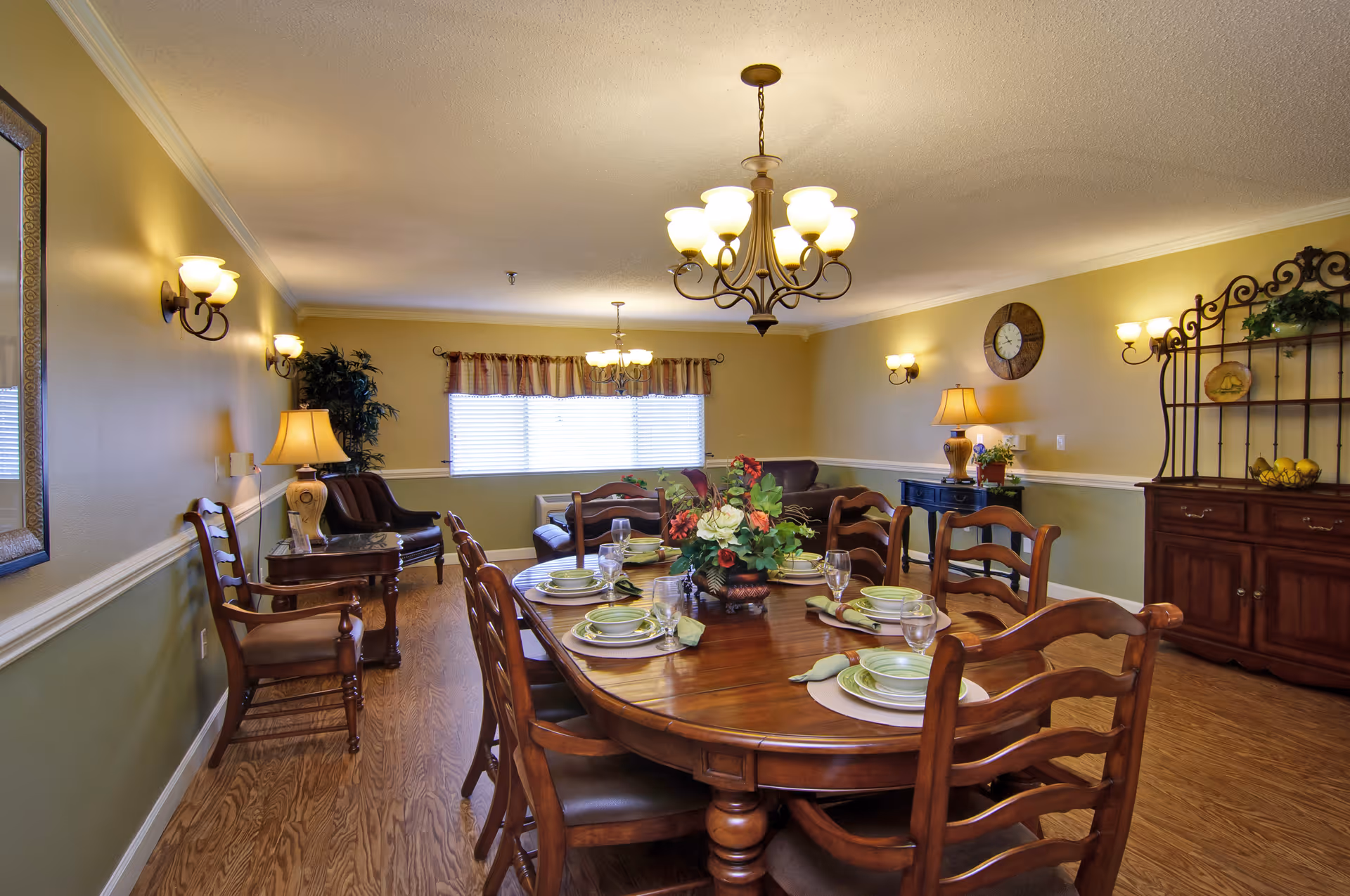 Well-lit dining room with a large wooden table set for a meal, chandelier overhead, and sideboard and seating in the background.