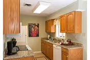 Well-lit galley kitchen with oak cabinets, granite countertops, white appliances, and a window above the sink.