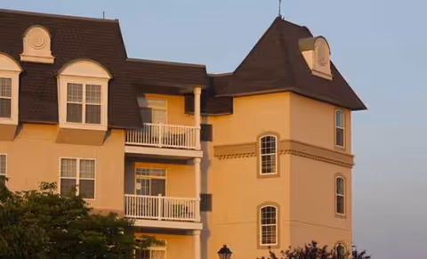 Exterior view of a multi-story senior living building with balconies and a turret roof.