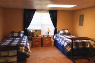 Two twin beds with plaid quilts flank central nightstands and lamps in a cozy beige bedroom.
