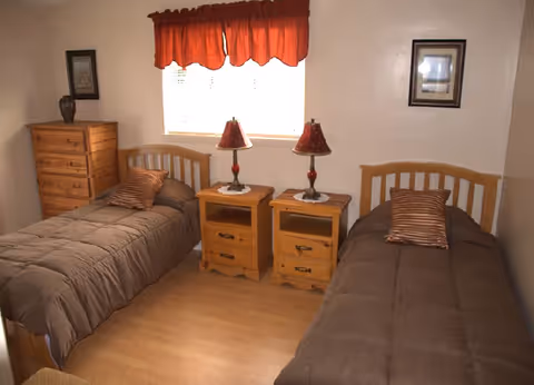 Two twin beds with matching nightstands and lamps in a small beige bedroom.