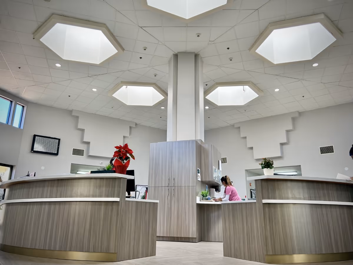 Modern interior reception area with curved wood-tone desks, a central column, hexagonal skylights, and a staff member working behind the counter.