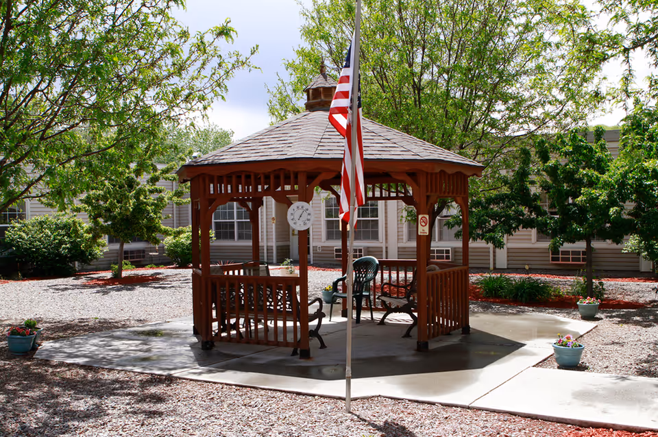 Wooden gazebo with benches and an American flag in a landscaped courtyard.