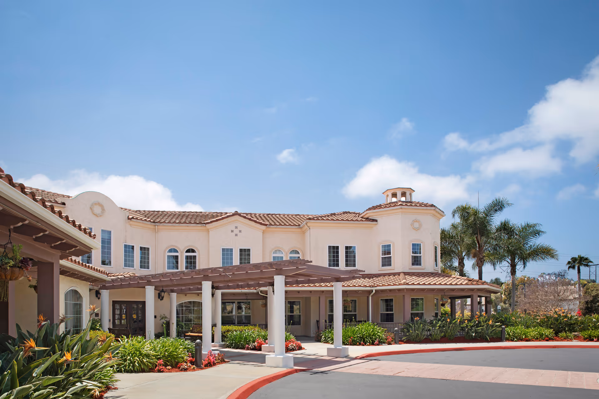 Sunny day exterior view of Sunrise at La Costa senior living facility, Mediterranean-style building with landscaping.