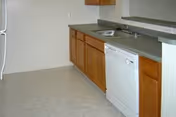 A small senior living facility kitchen with wooden cabinets, sink, dishwasher, and counter space.