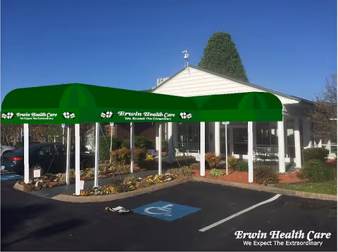 Entrance of Erwin Health Care Center with a green awning over a walkway, handicap parking space, and landscaped beds.