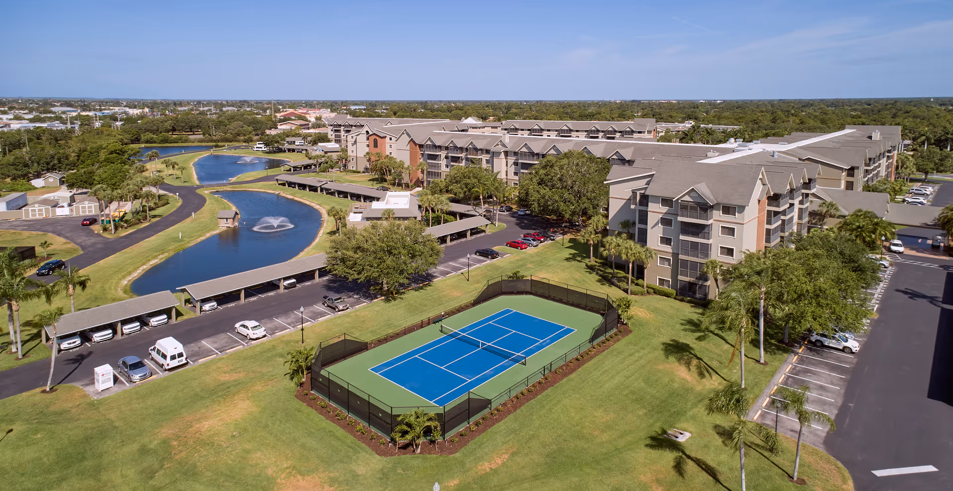 Aerial view of South Port Square senior living campus with buildings, pond, and tennis court.