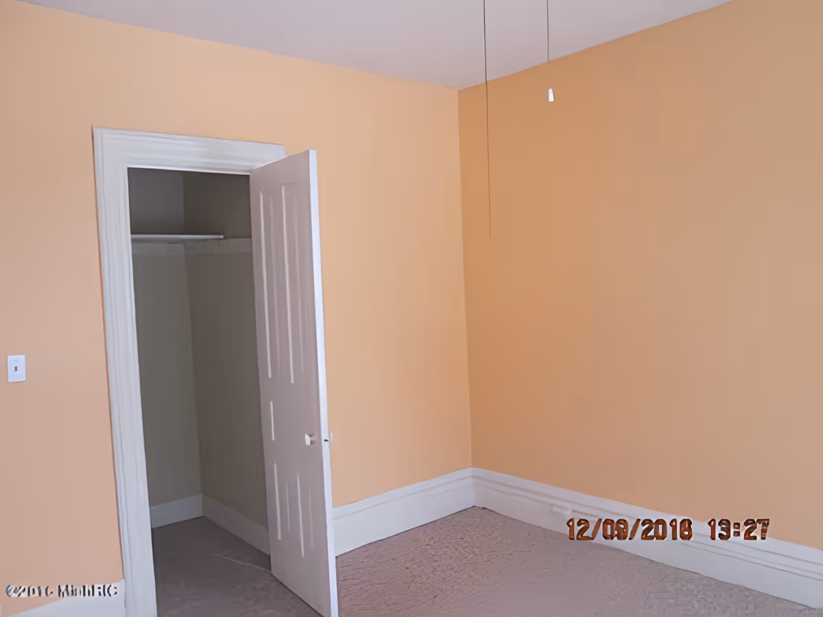 Empty peach-painted bedroom corner with an open closet door and carpeted floor.