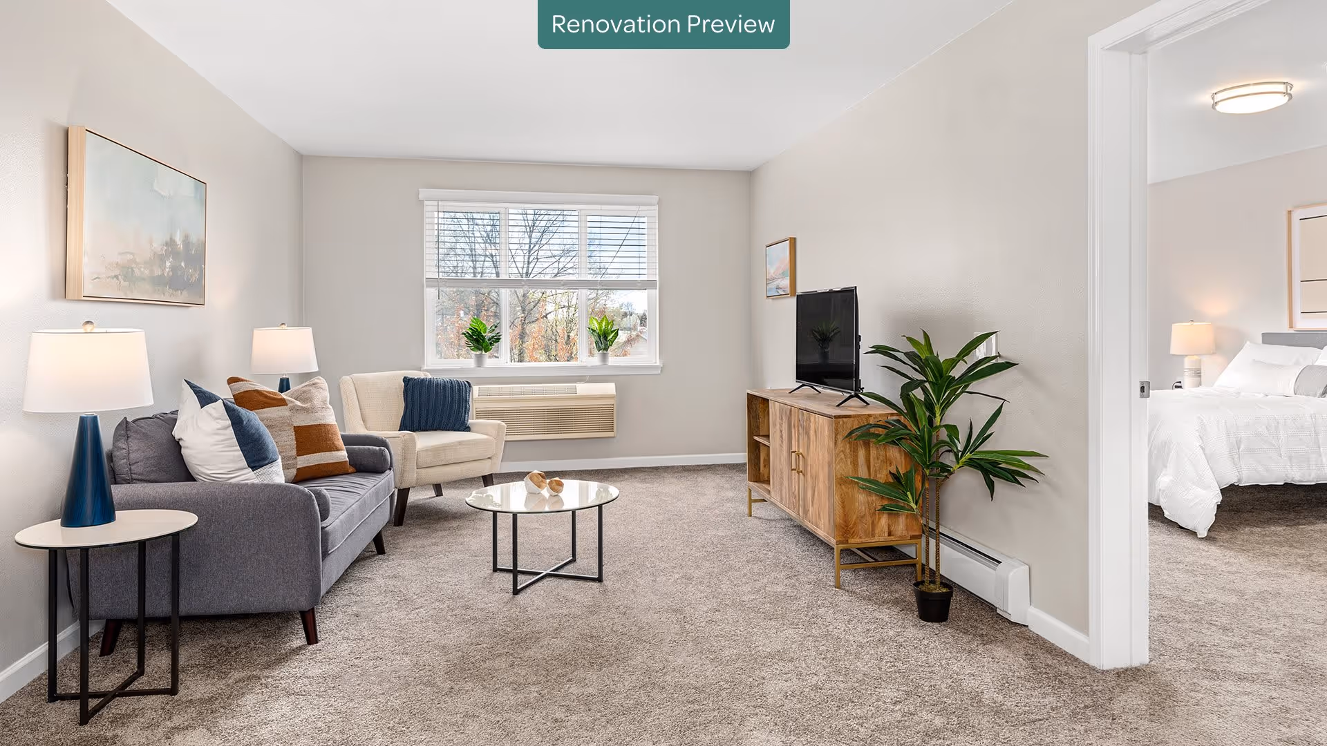Bright furnished living room with a sofa, armchair, coffee table, TV stand, and a view into a bedroom.