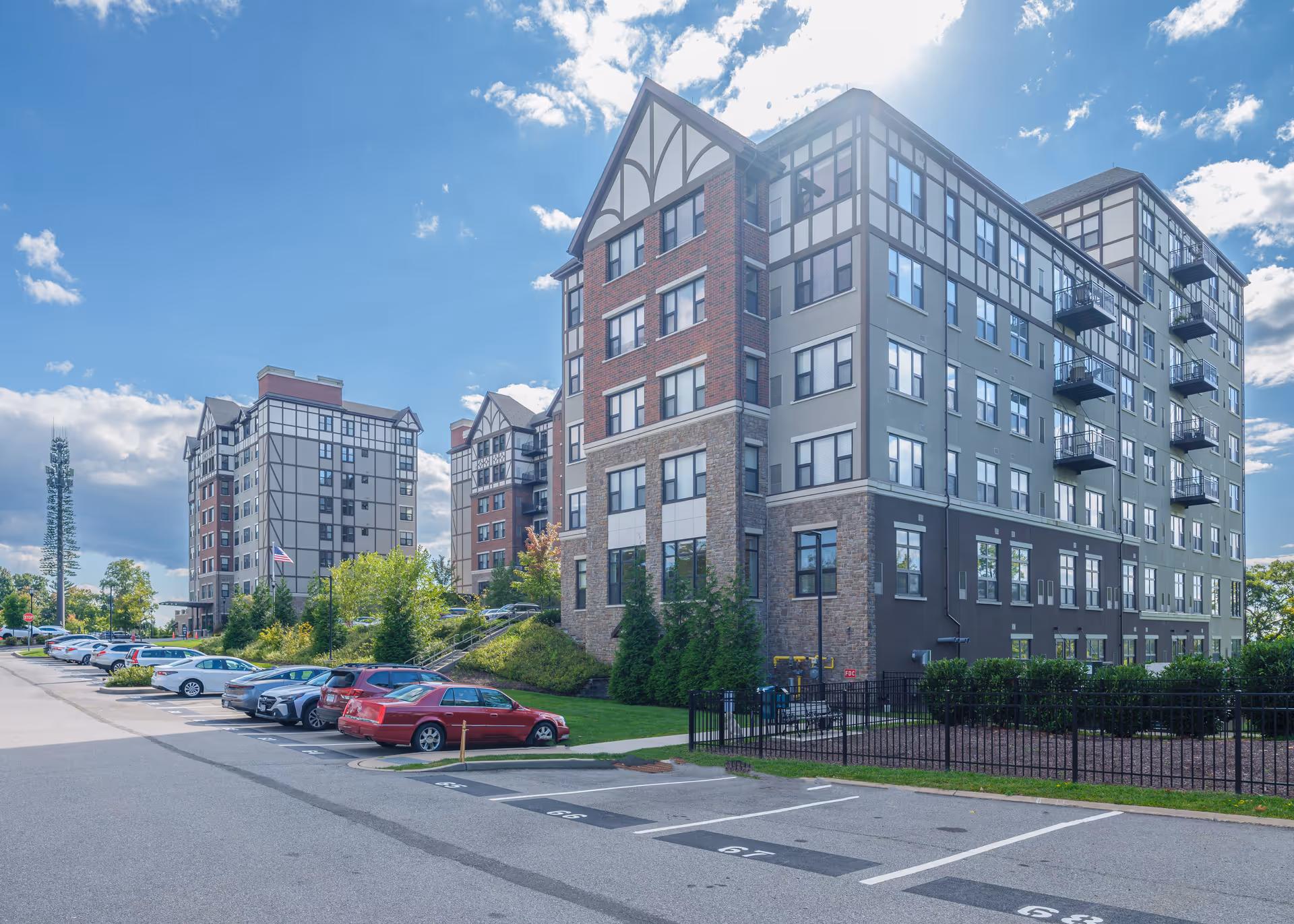 Exterior view of a multi-story senior living apartment complex with parked cars and landscaped grounds under a blue sky.