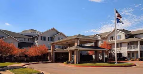 Exterior view of Holiday Grasslands Estates senior living facility with a covered entrance and autumn trees.