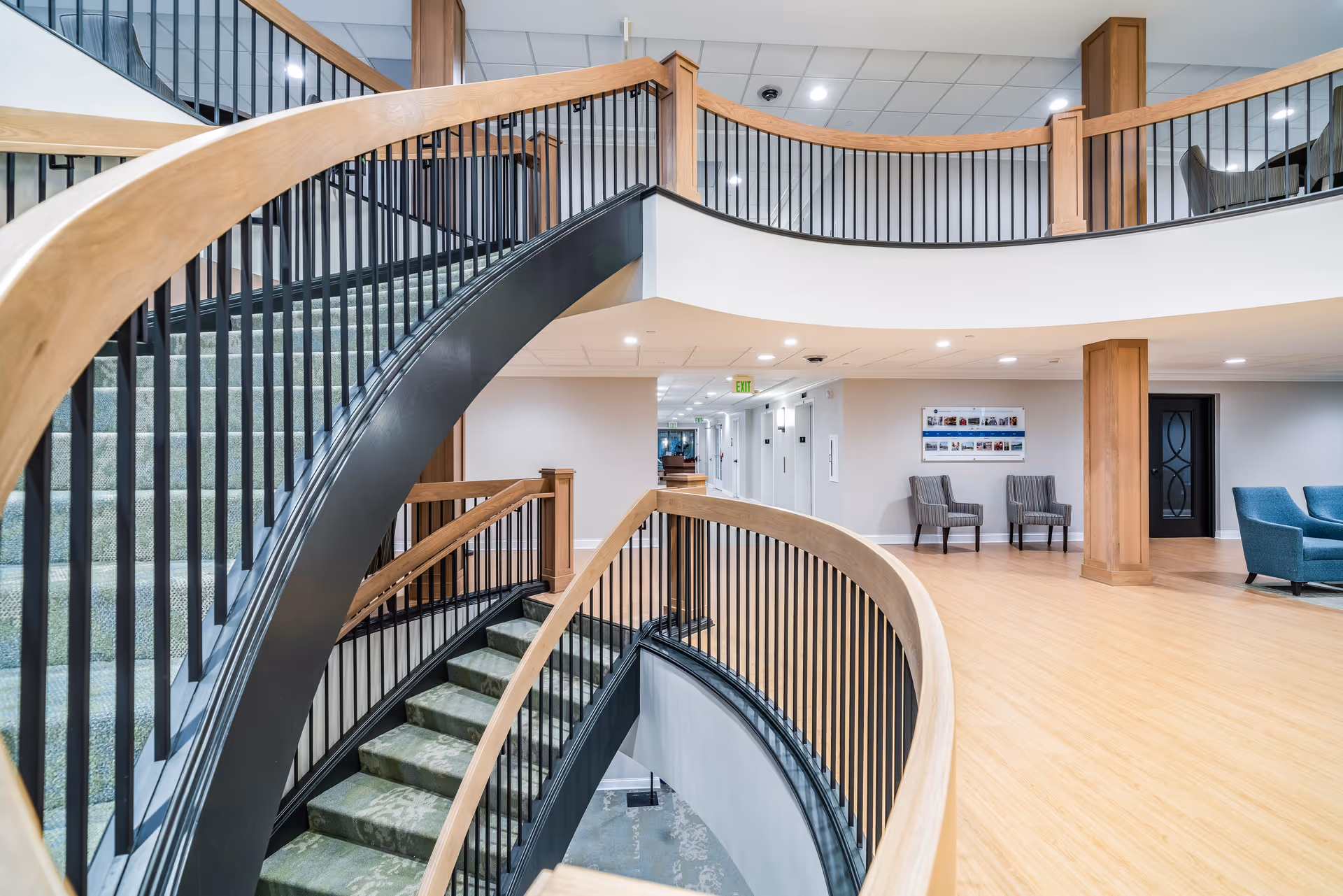 Interior view of a multi-level stairwell with curved railings and seating areas in a senior living facility.