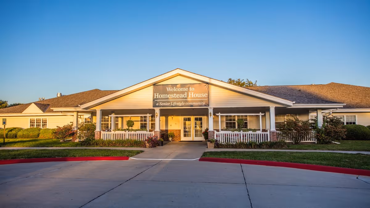 Front entrance of Homestead House senior living facility with a covered porch and welcome sign.