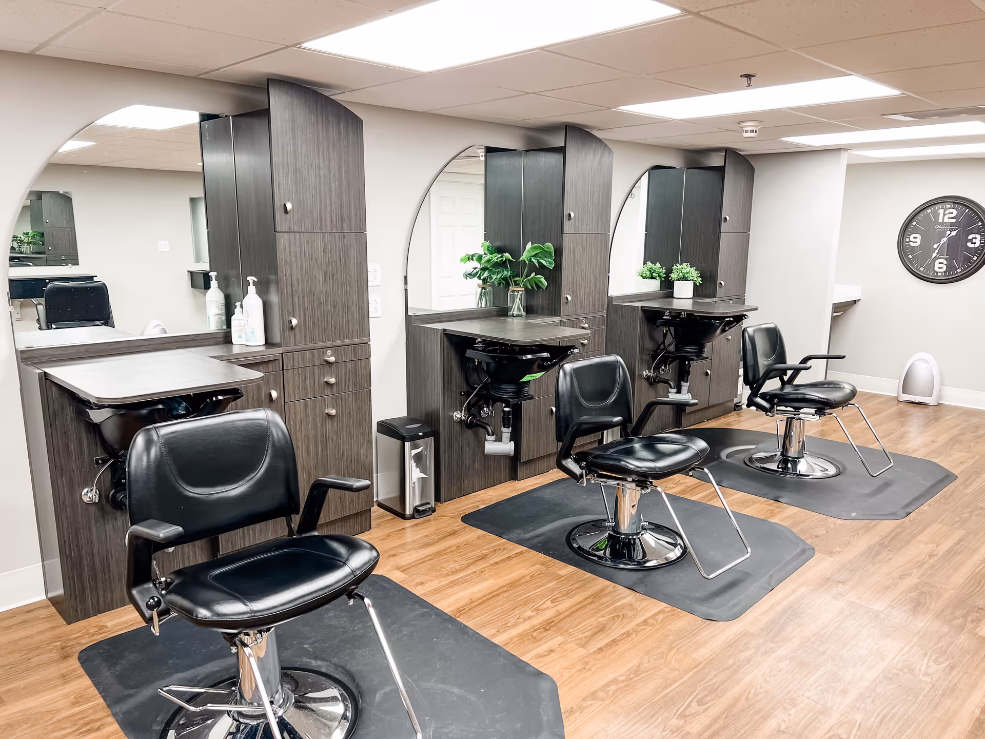 Interior salon with three styling stations, black salon chairs, sinks, mirrors, and wood cabinets.