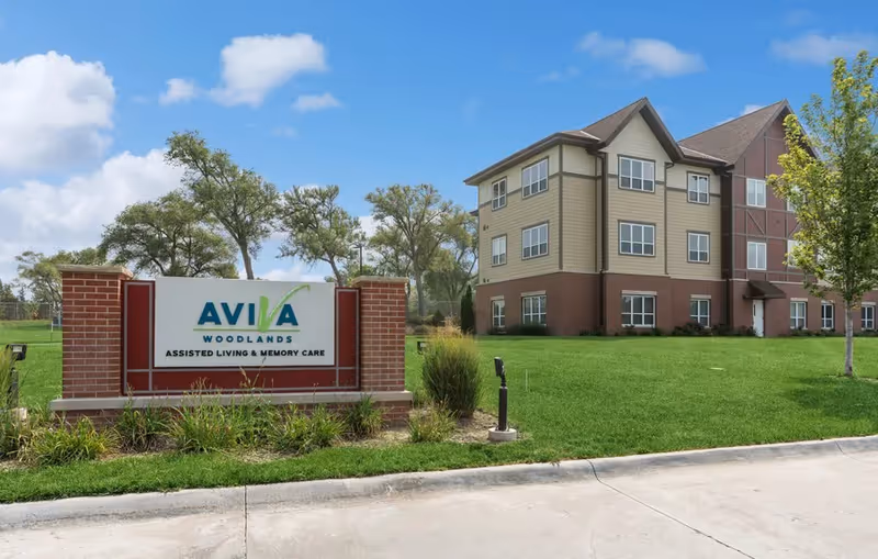 AVIVA Woodlands assisted living building and sign on a green lawn under a blue sky.