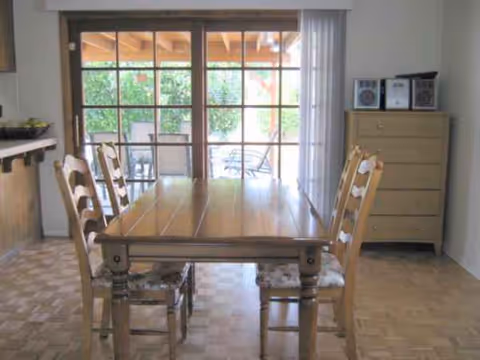 Wooden dining table with chairs in a bright dining room with sliding glass doors.