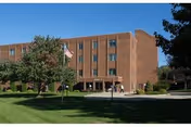 Brick senior living building with entrance, flagpole, and well-kept lawn in front.