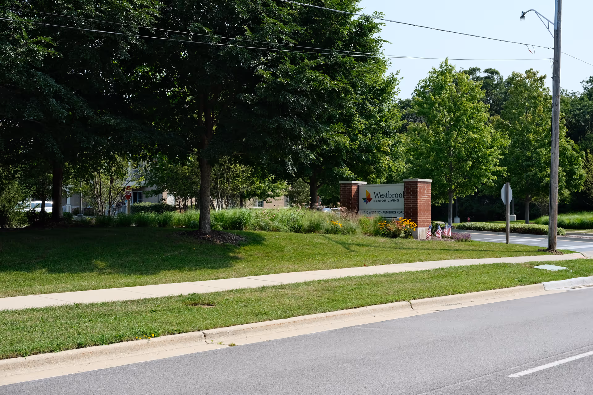 Roadside entrance sign for Westbrook Senior Living set among trees, lawn, and landscaping.