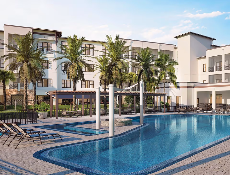 Outdoor swimming pool area at Siena Lakes Senior Living Community with lounge chairs, palm trees, pergolas, and a multi-story building in the background under a partly cloudy sky.