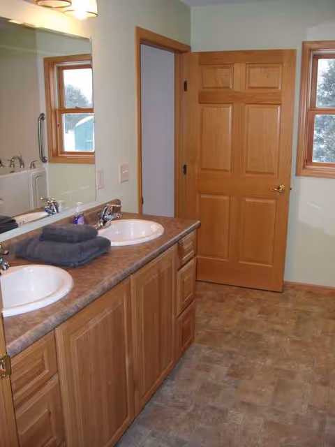 Double-sink bathroom vanity with wooden cabinets, mirrors, towels, and a door.