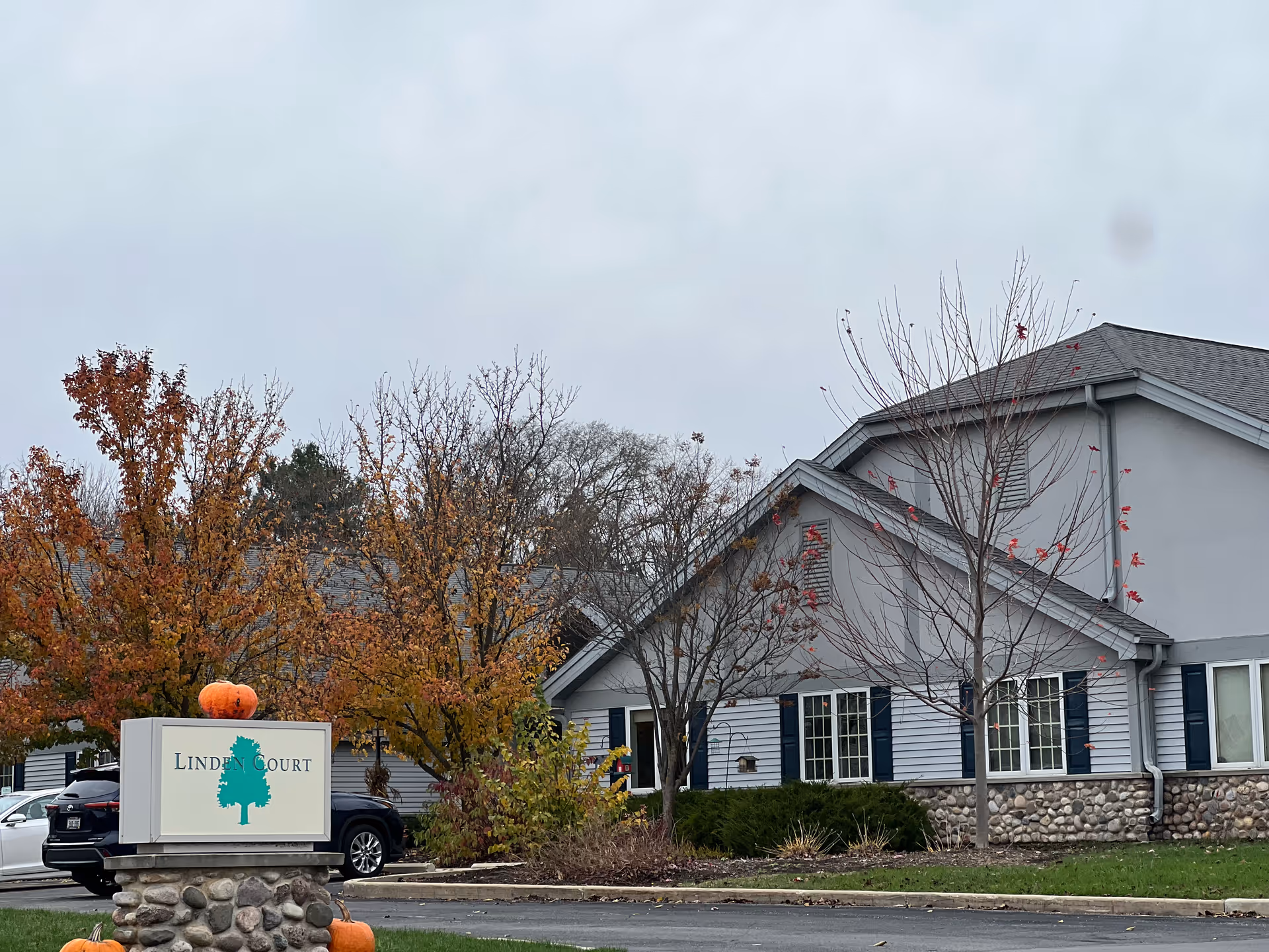 Front exterior of the Linden Court building with its sign, pumpkins on the signpost, and autumn trees in the landscaping.