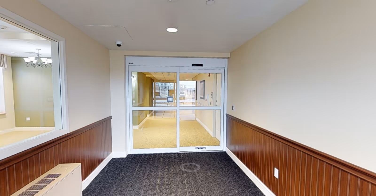 Interior view of the entrance hallway at Laurel Run Personal Care, featuring a glass door, carpeted floor, and wooden paneling along the walls.