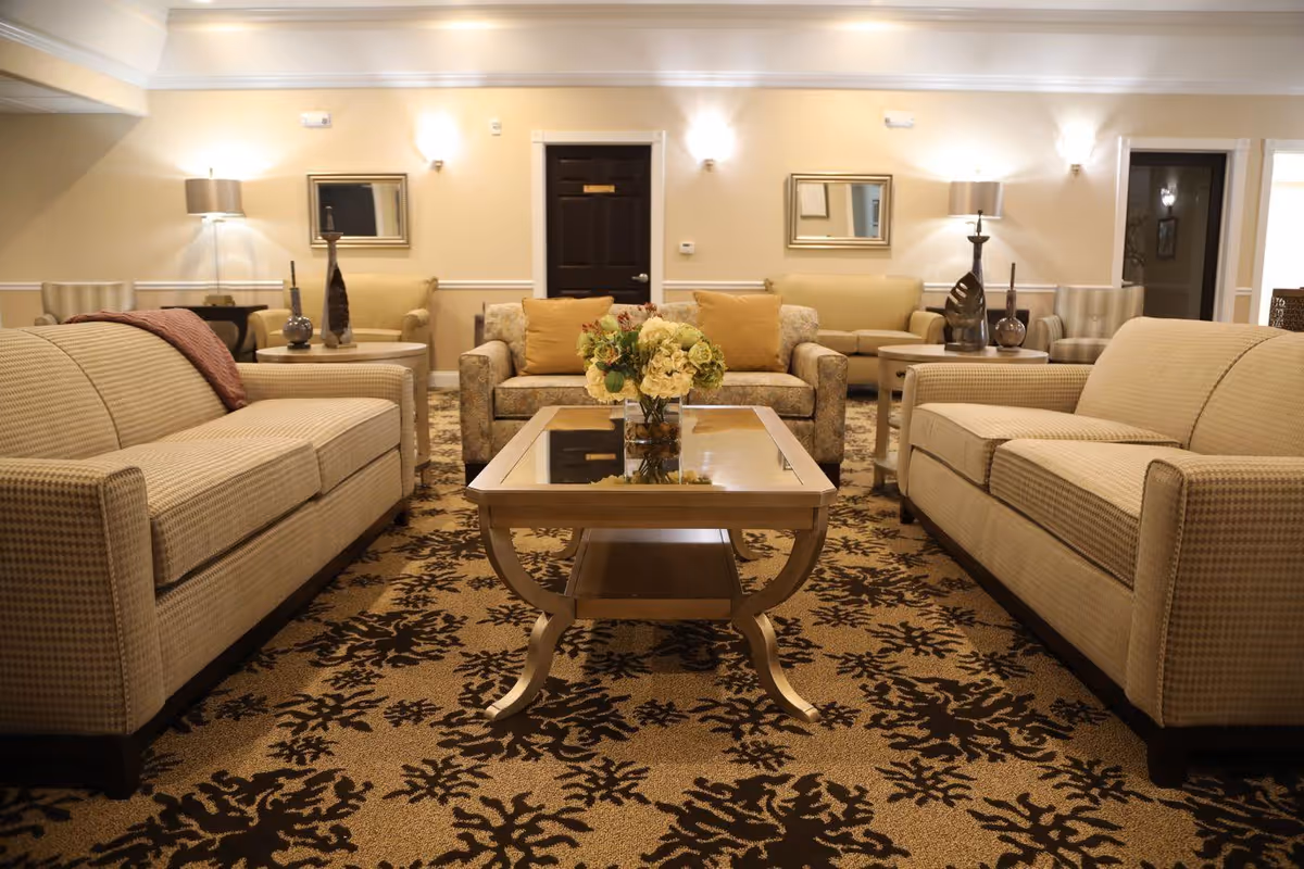 Well-lit communal living room with sofas arranged around a central glass-top coffee table topped with a floral arrangement.