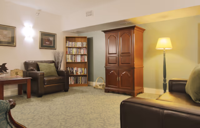 Cozy living room with leather armchairs, a wooden armoire, bookshelf, and a floor lamp.