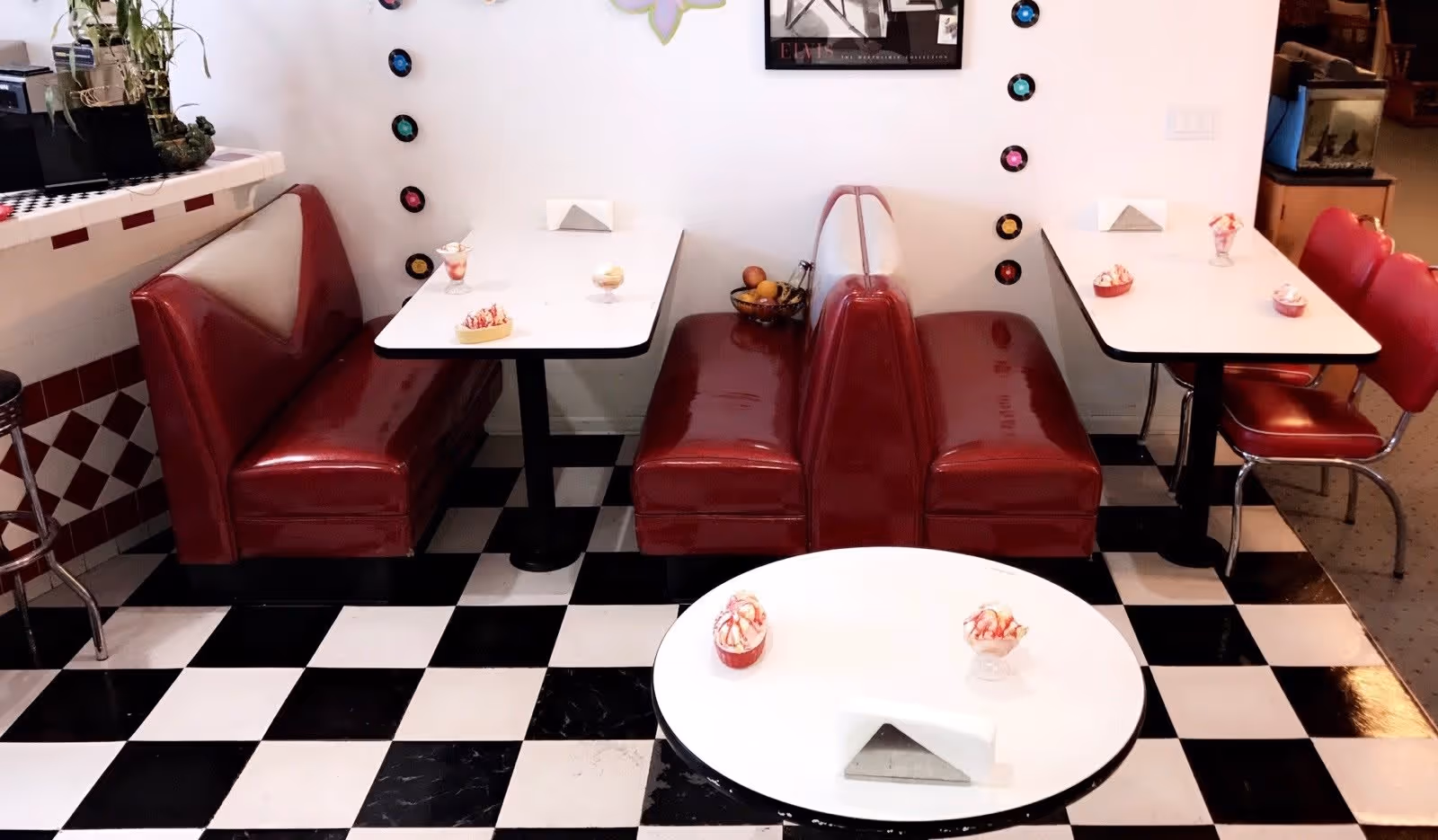 Retro diner-style seating with red vinyl booths and white tables on a black-and-white checkered floor, small dessert dishes on the tables.