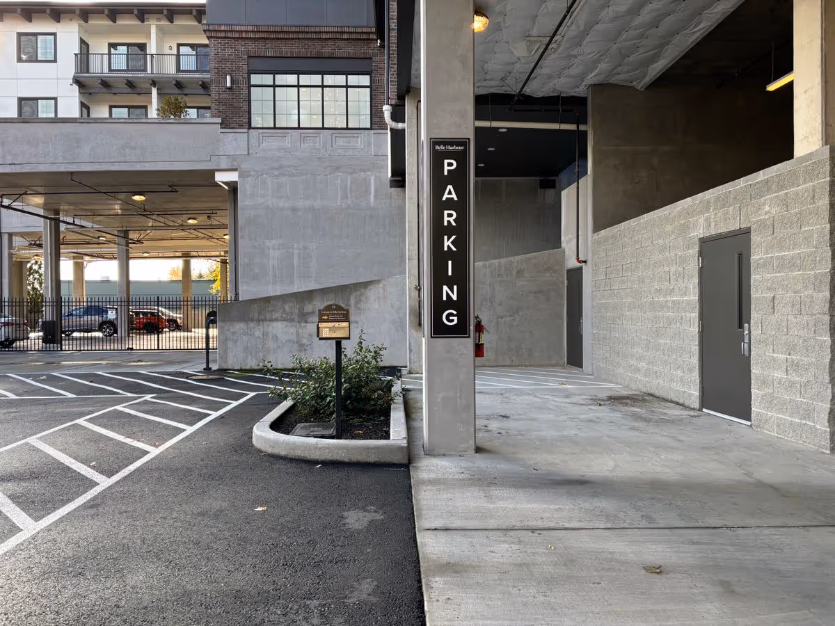 Covered building exterior showing a parking entrance with a vertical 'PARKING' sign and marked parking lanes.