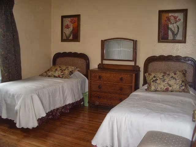 A bedroom with two twin beds, a wooden dresser with a mirror, floral pillows and framed artwork on the walls.