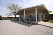 Front entrance of a single-story care center with a covered portico supported by white columns, a driveway, and landscaping.