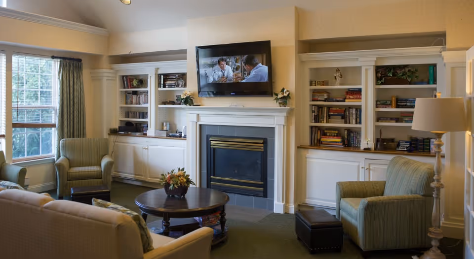 Cozy living room with a fireplace, wall-mounted TV, built-in bookshelves, armchairs, and a coffee table.