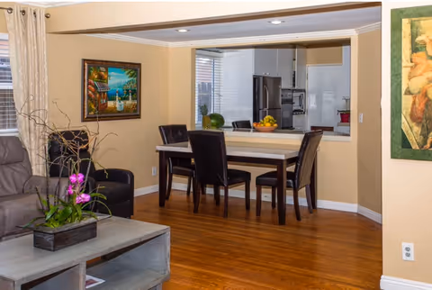 Open-plan living and dining area with a wooden table and chairs, hardwood floors, and a view into the kitchen.