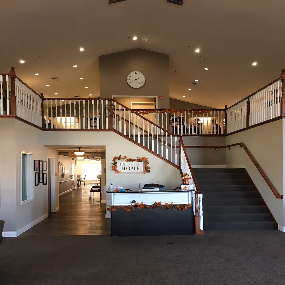 Two-story lobby with staircase, railings, a clock, and an autumn-themed reception desk.