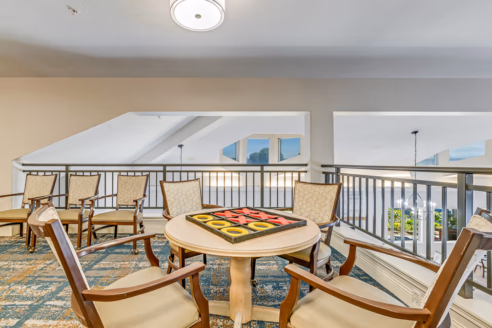 Upstairs common seating area with a round game table and several chairs overlooking a lower-level atrium.