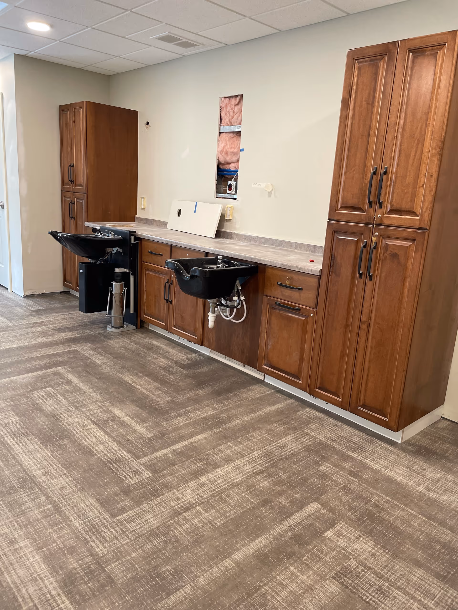 Two black salon shampoo sinks set into wooden cabinetry along a wall in an interior room with patterned flooring.