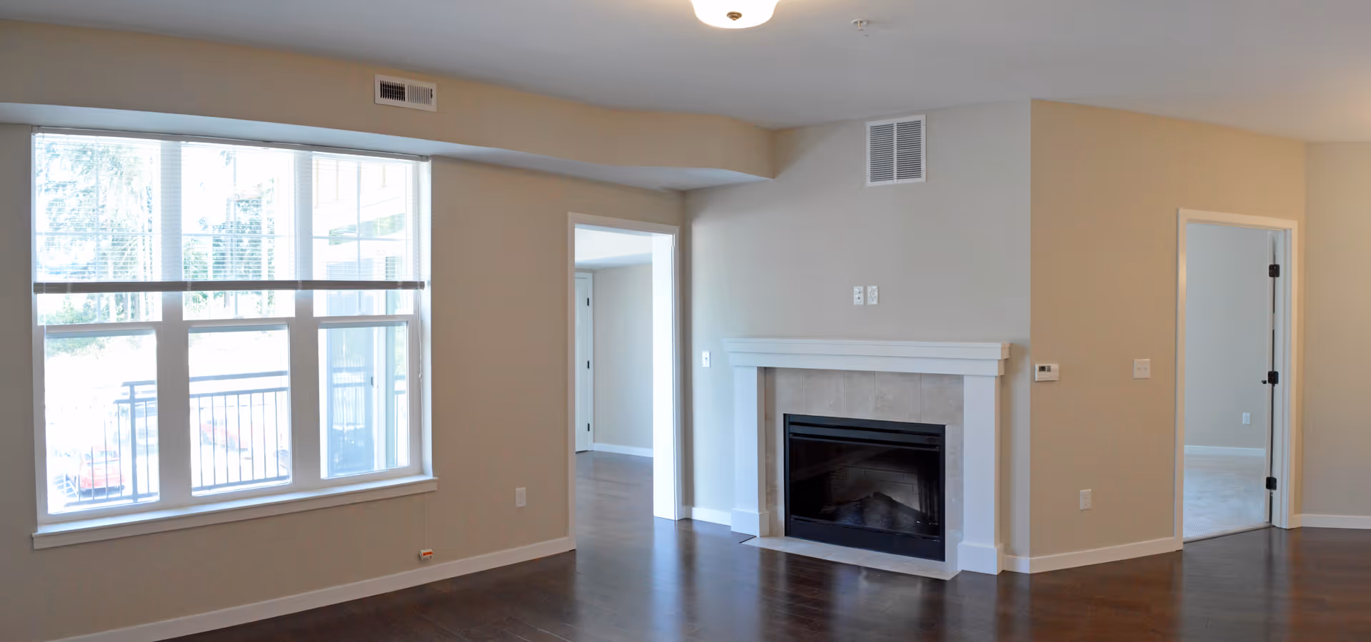 Bright empty living room with large windows, hardwood floors, and a fireplace.