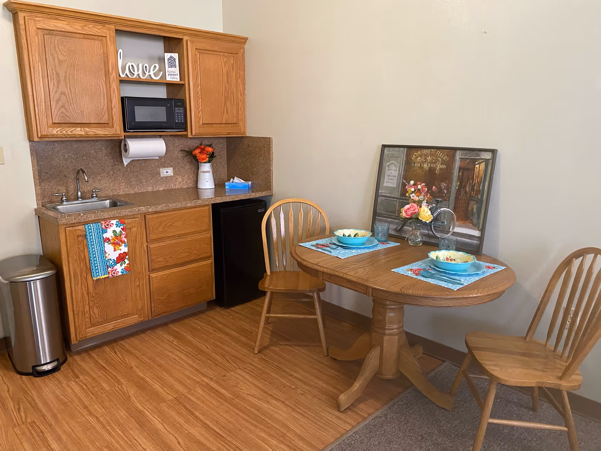 Compact kitchen and small dining nook with wooden table and chairs in a senior living unit.