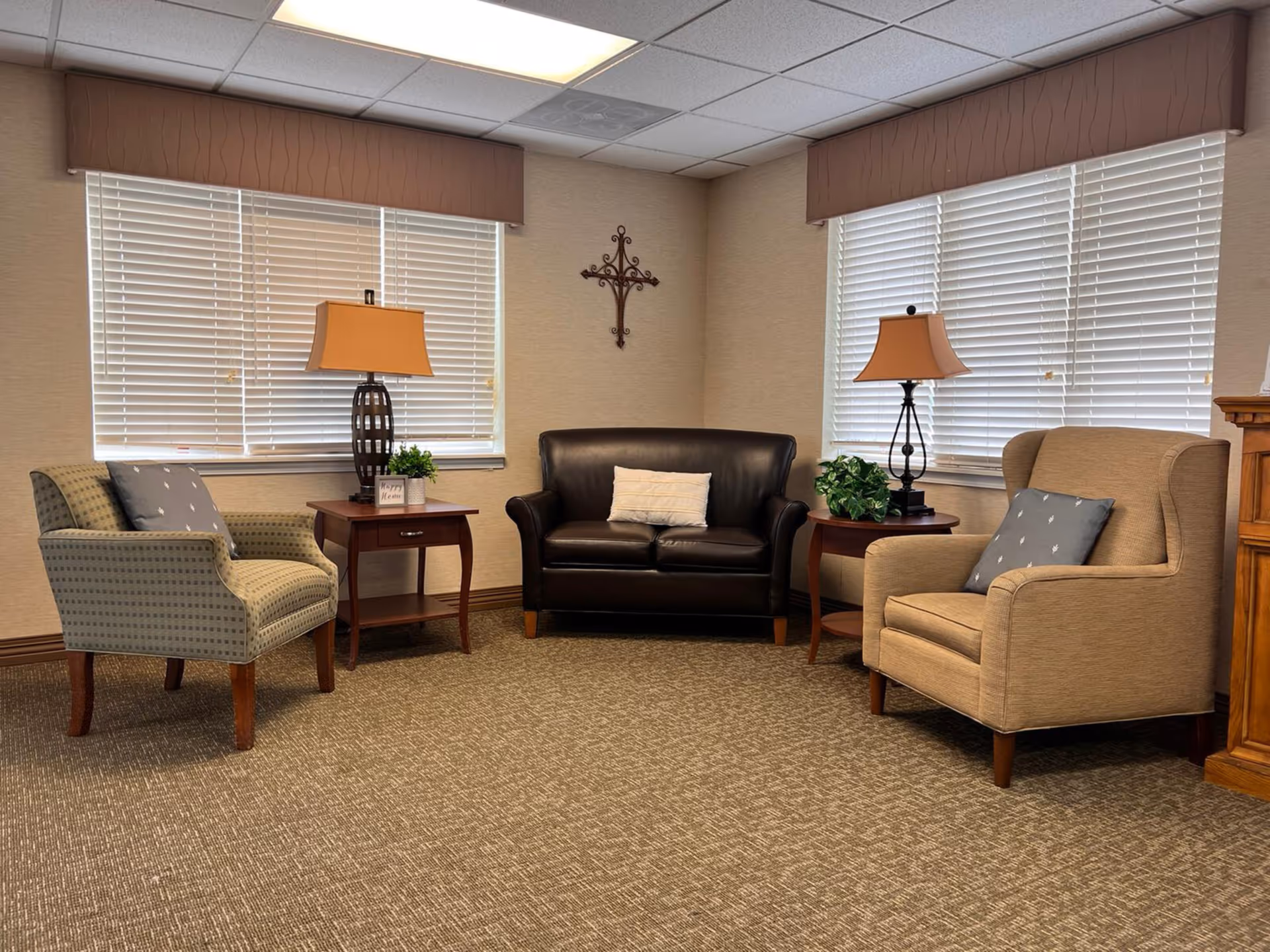 Small communal lounge with two upholstered armchairs, a leather loveseat, side tables with lamps, and window blinds.