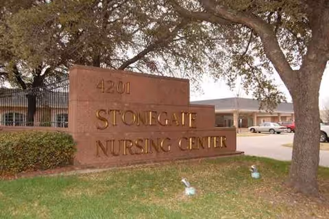 Exterior view of Stonegate Nursing Center sign at the entrance and parked cars nearby.