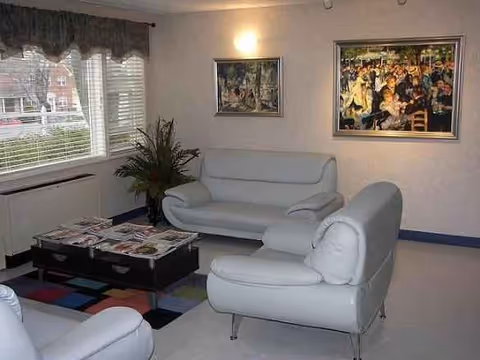 Light lounge area with white leather couches, coffee table, plant, and framed artwork.