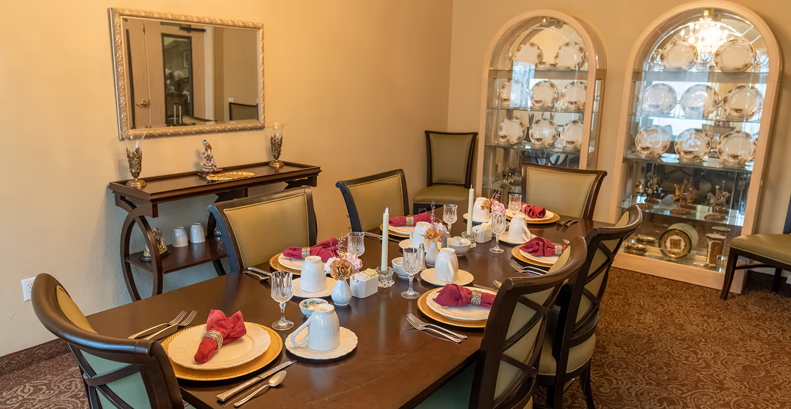 A formal dining room with an elegantly set wooden table for eight, china cabinets, and a mirror-topped sideboard.