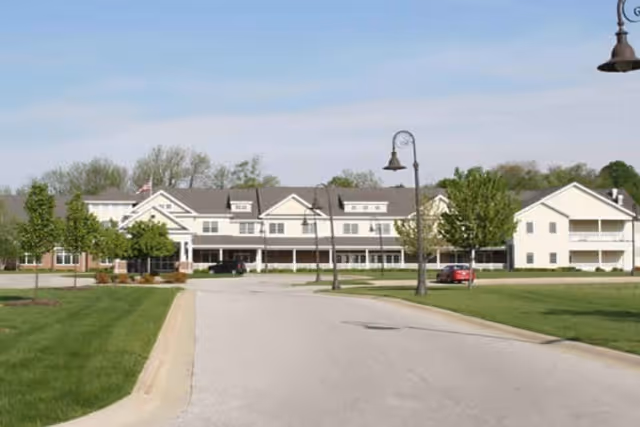 Front exterior view of the Hamilton Grove senior living building with a driveway, lawn, street lamps, and parked cars.