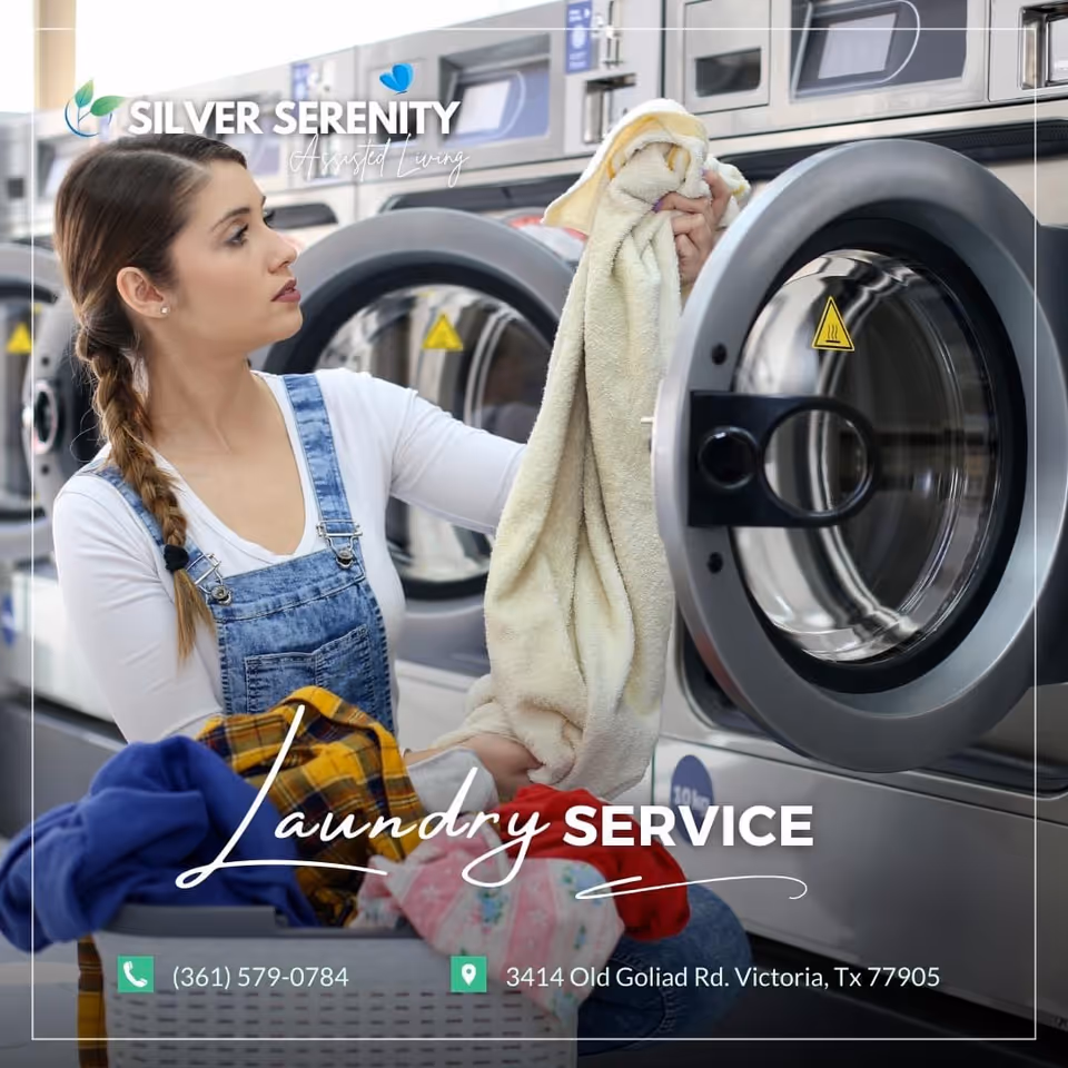 A woman with braided hair wearing a white long-sleeve shirt and denim overalls is taking a towel out of a front-loading washing machine in a laundry room. There are multiple washing machines in the background and a laundry basket with clothes in front of her. The image has text overlay promoting laundry service at Silver Serenity Assisted Living Victoria.