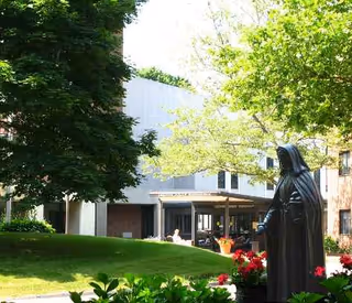 Exterior view of Jeanne Jugan Residence with statue, trees, and a building entrance.