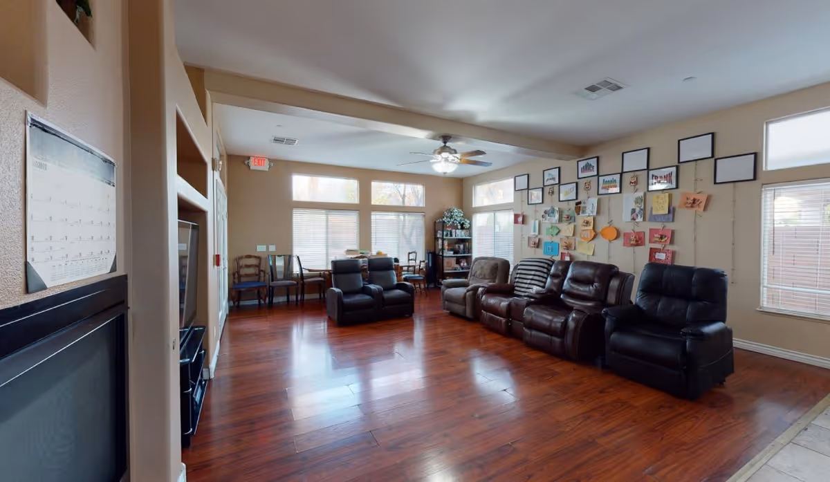 Bright common lounge with several leather recliners, hardwood floors, windows, and a wall display of artwork.