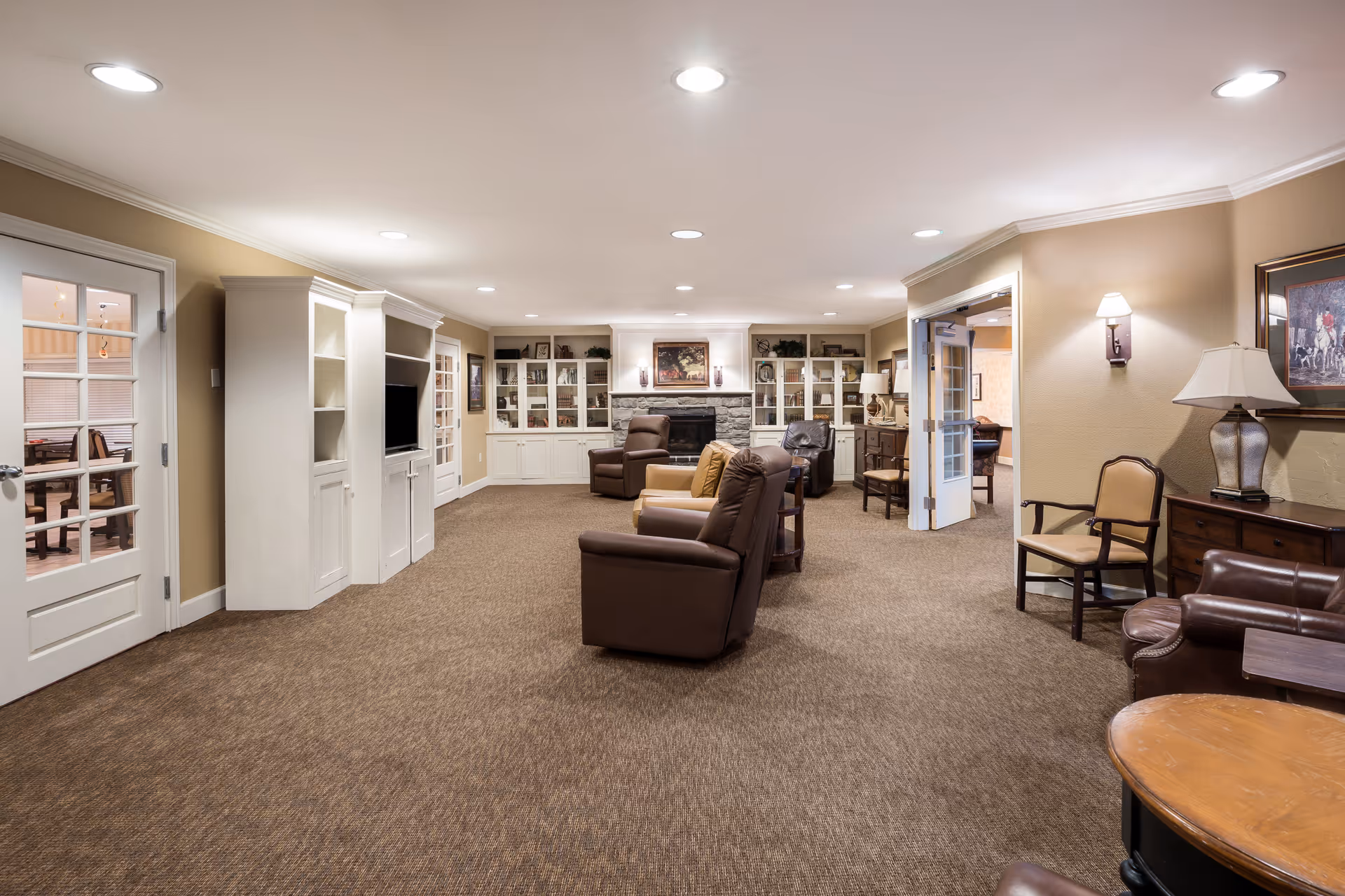 Spacious furnished communal living room with recliners, built-in shelving, and a fireplace.