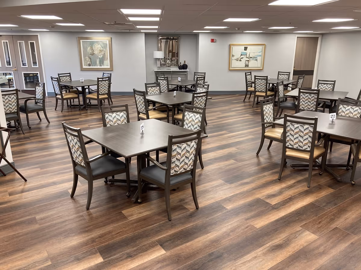 Spacious dining room with multiple square tables and patterned chairs on wood-look flooring.